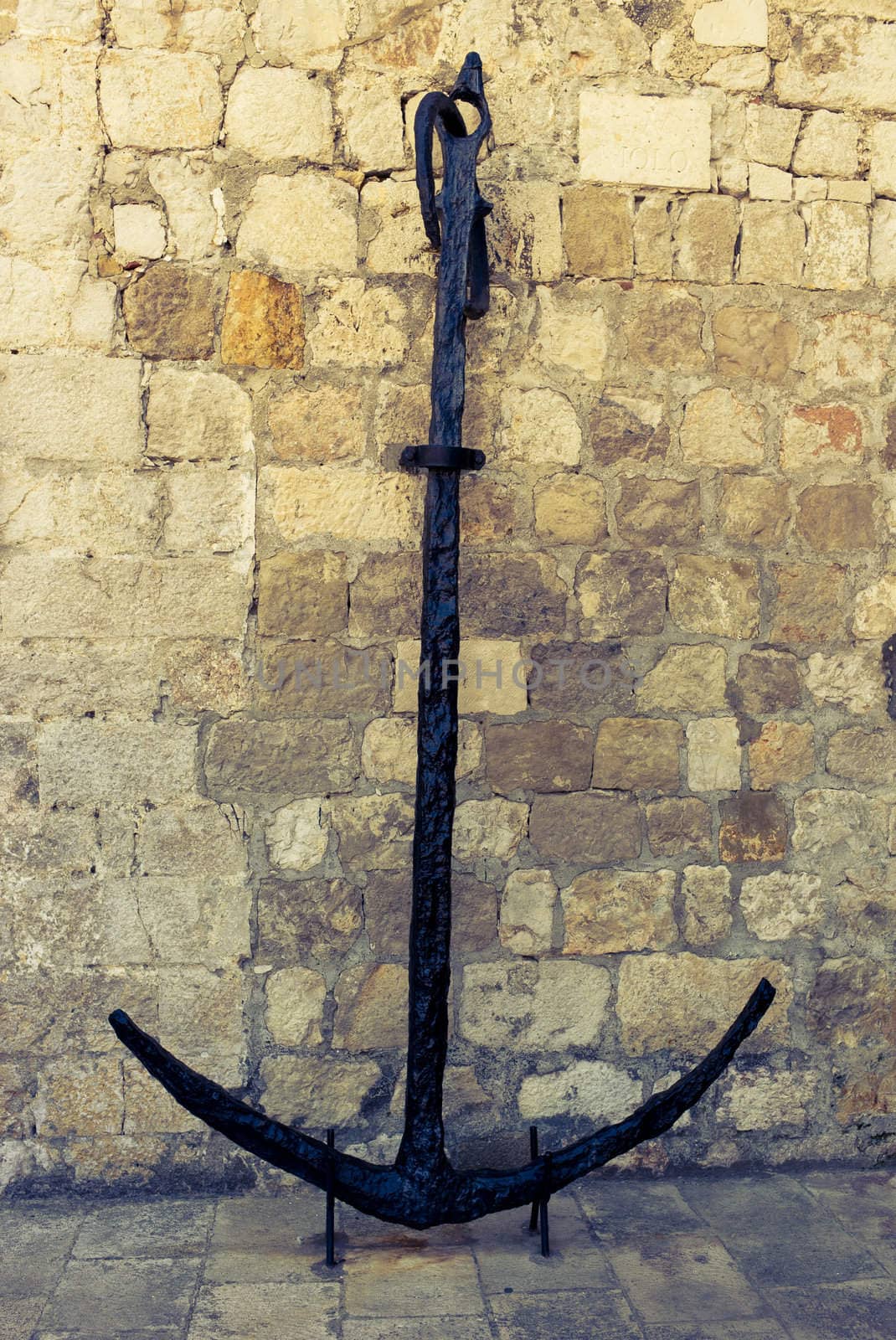 A vintage Croatian anchor in front of stone wall. Image is cross processed to reflect time and age.