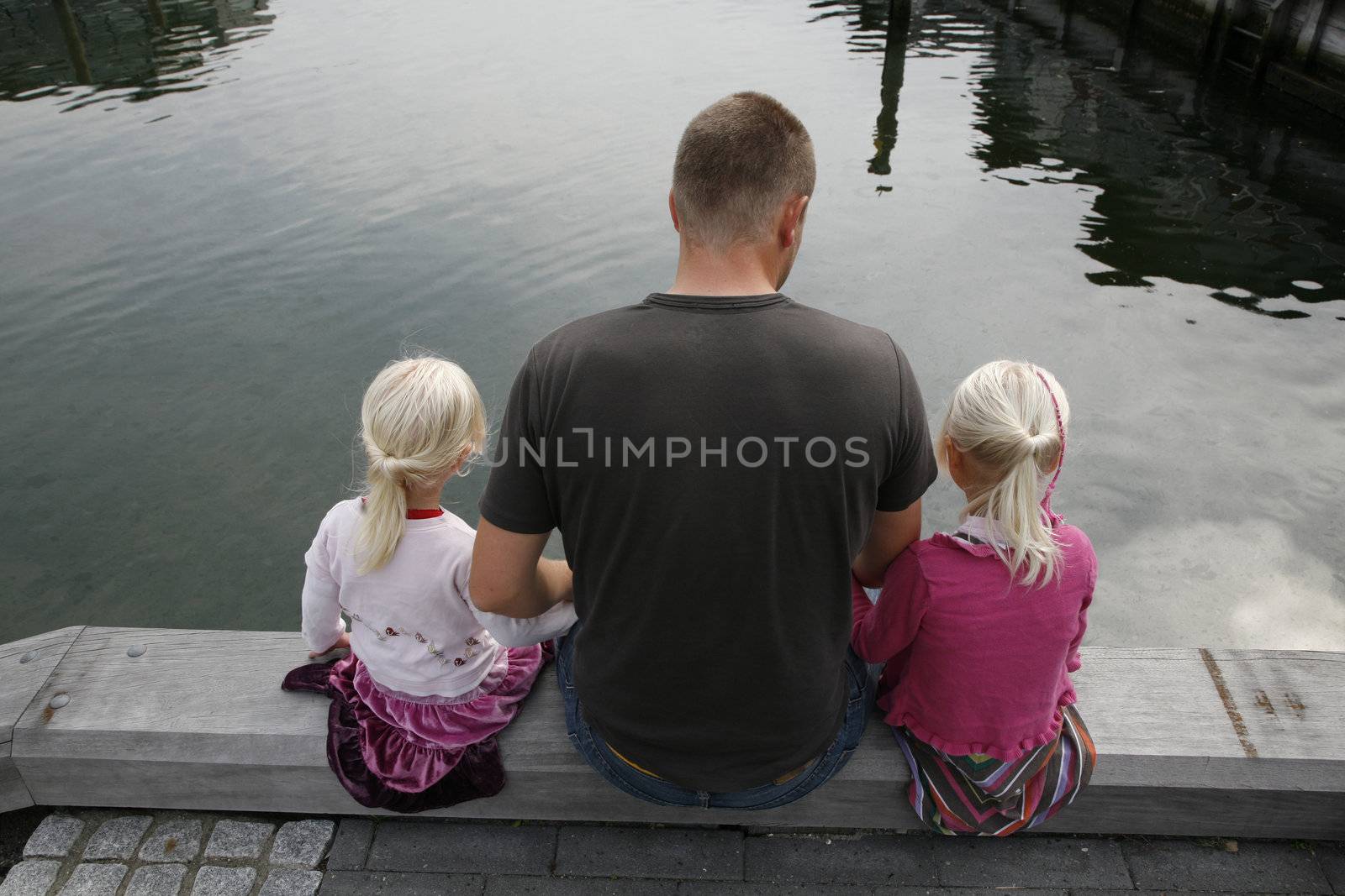 Father with his two small girls sitting looking for fish in the water.