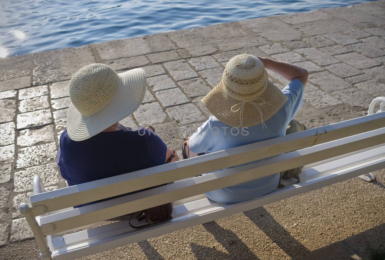 Two elderly females sitting and enjoying their vacation on a bench in the sun - Croatia.
