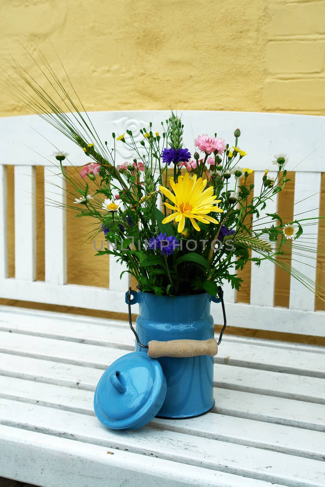 Beautiful spring summer flowers in a blue tin bucket on a garden bench vertical image