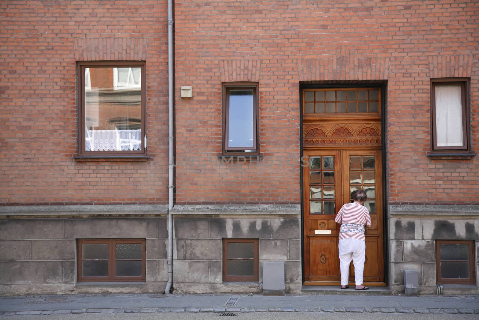 Senior female cleaning the frontdoor of an old weathered urban apartment building.