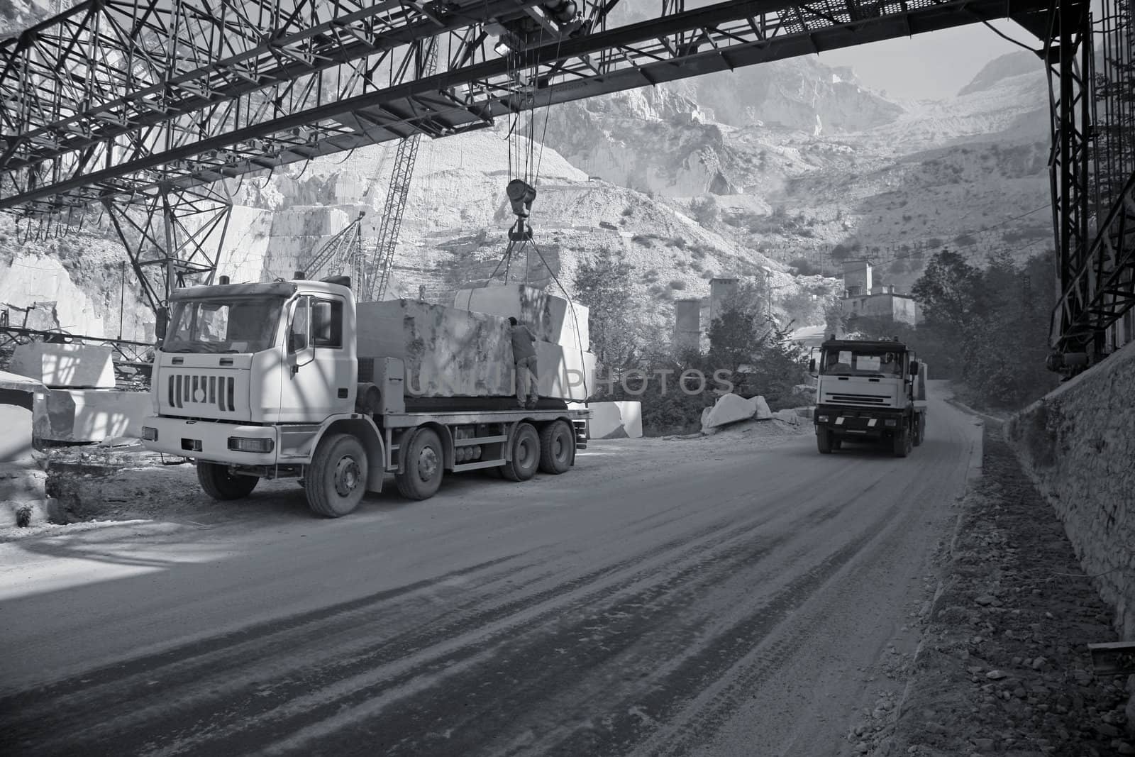 Marble quarry in the mountains near Carrara - Tuscany - Italy. A lorry is being loaded with big blocks of marble for transport whie another one is passing.