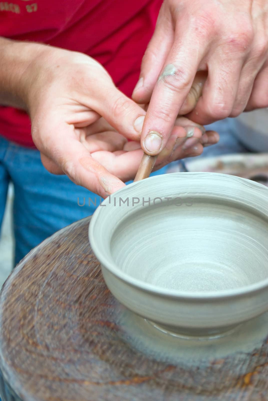 A potters hands guiding a child hands to help him to work with the ceramic wheel