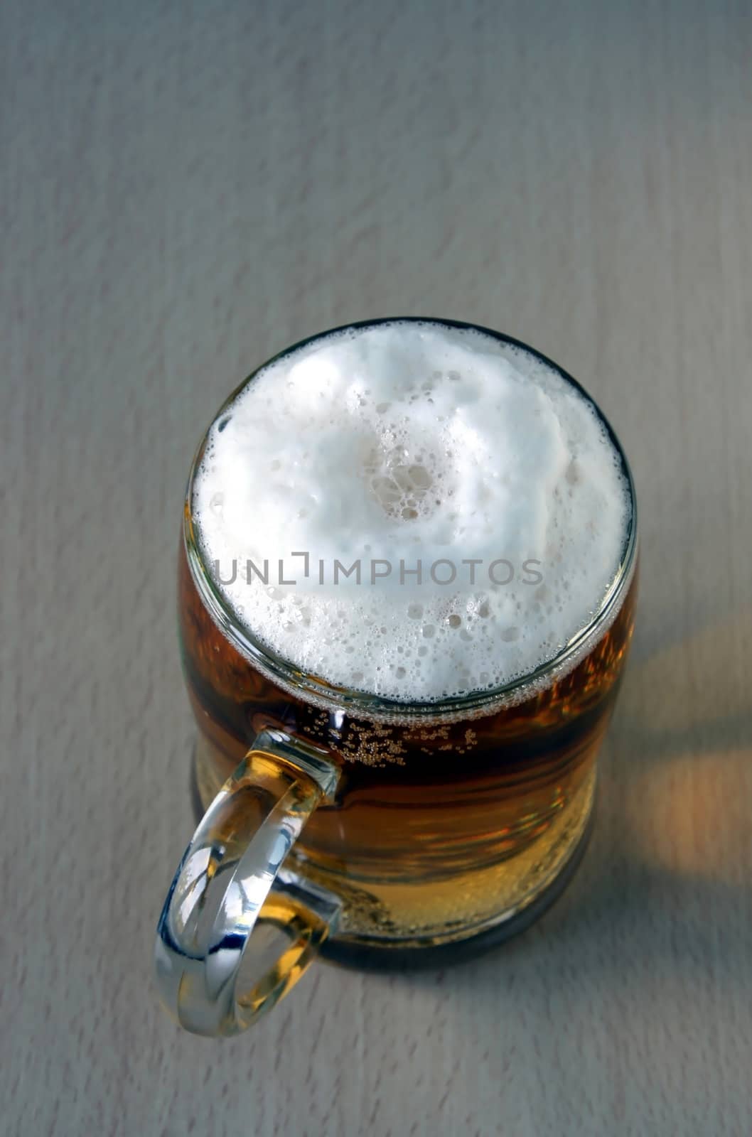 The full glass with foaming beer costs on a wooden table. The top point of shooting.