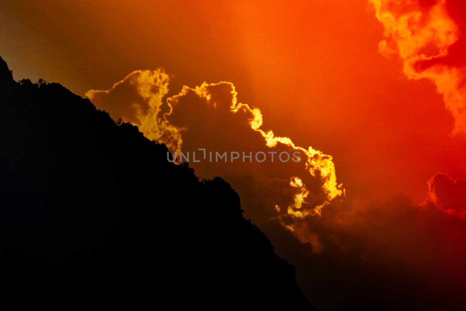 Rugged mountain silhouette and dramatic sunset sky with clouds.