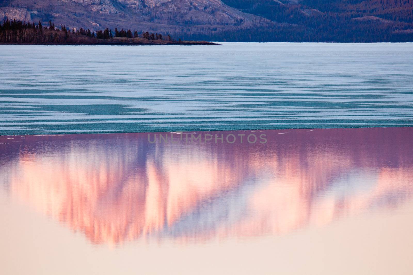 The evening before ice-break at Lake Laberge, Yukon Territory, Canada: reflection of snow-covered Mt. Laurier on calm open water surface of still largely ice-covered lake.
