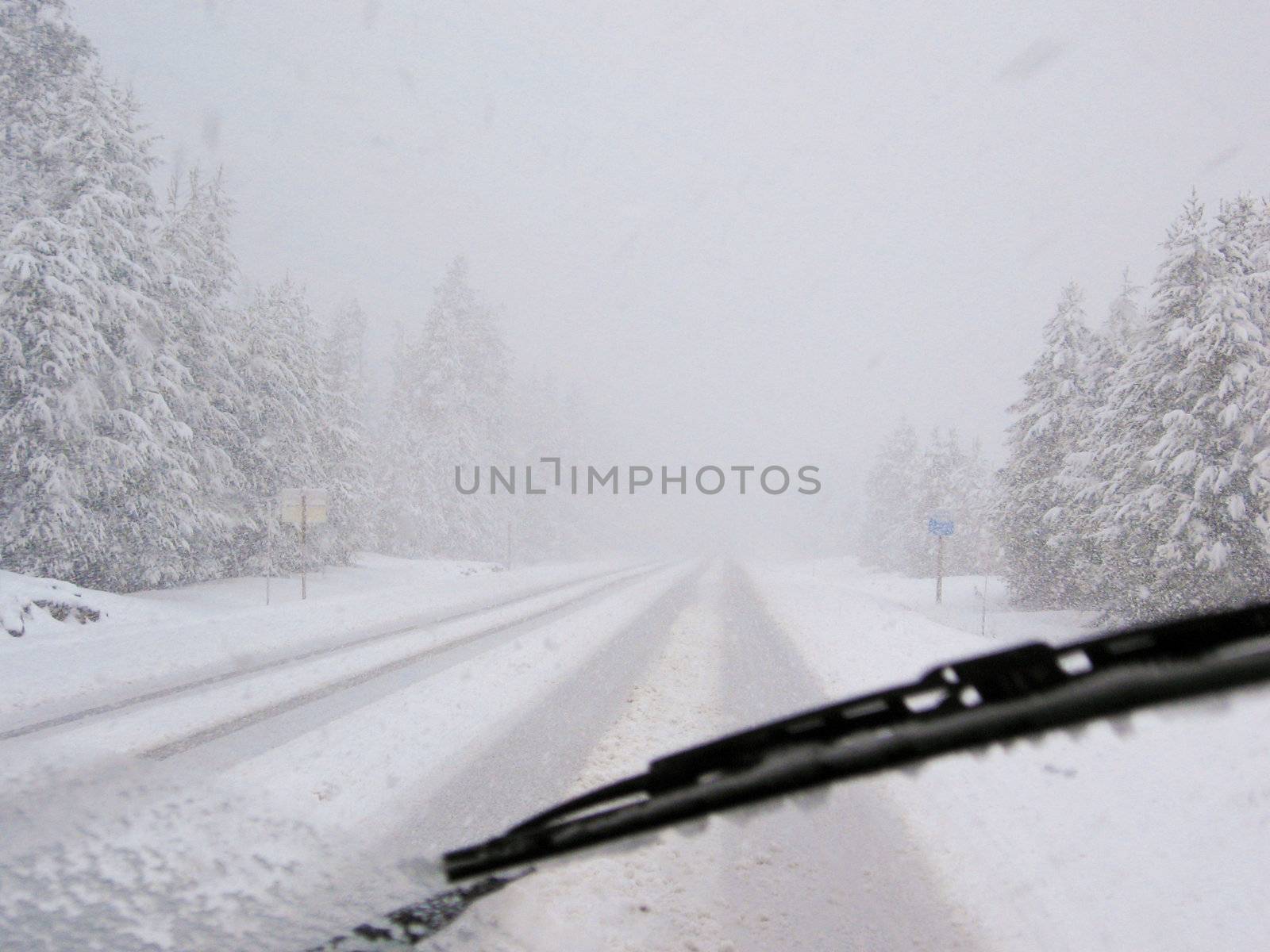 Dangerous driving conditions during blizzard on rural highway seen through car windshield.