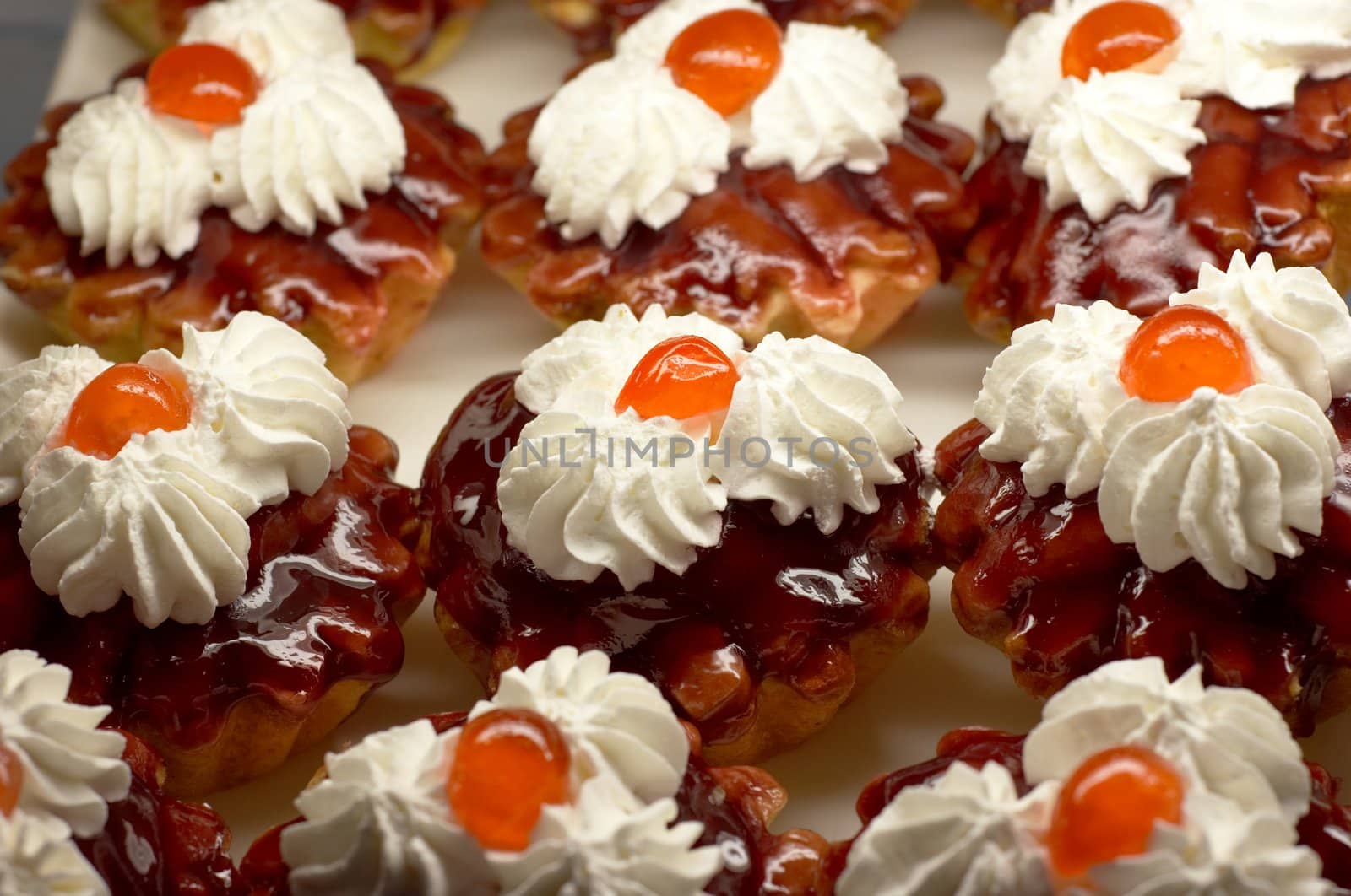 Small cupcakes with white cream and cherry on top. Shallow DOF.