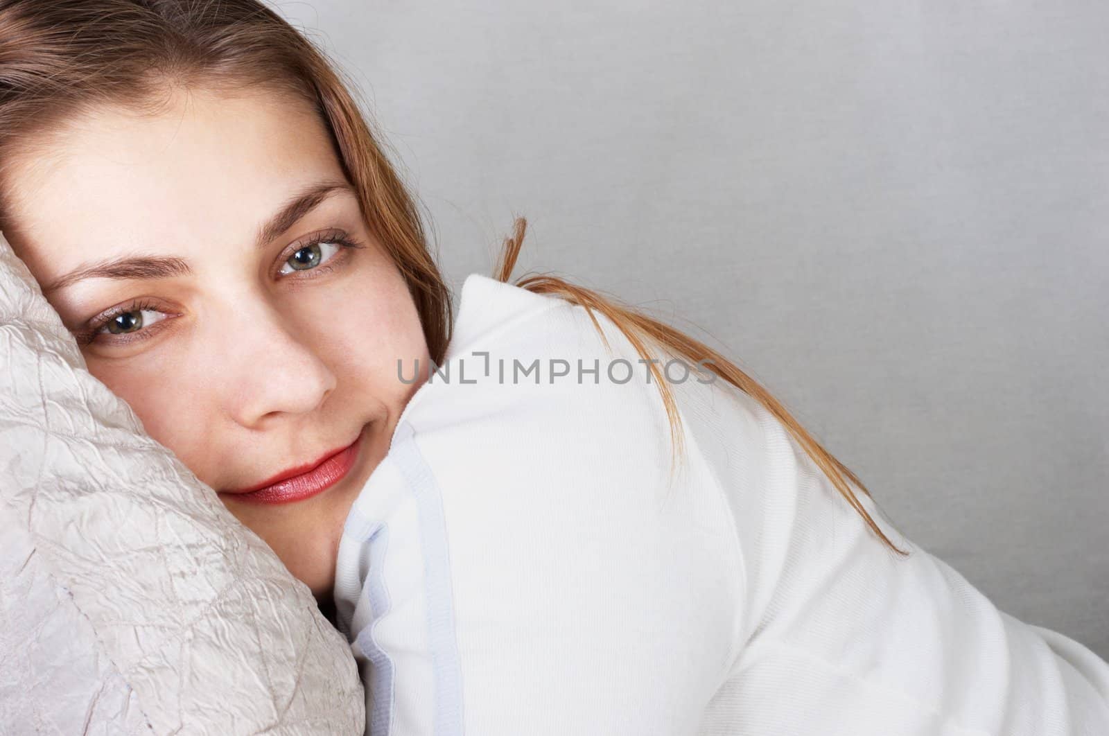 Daydreaming young girl in white lying on pillow.