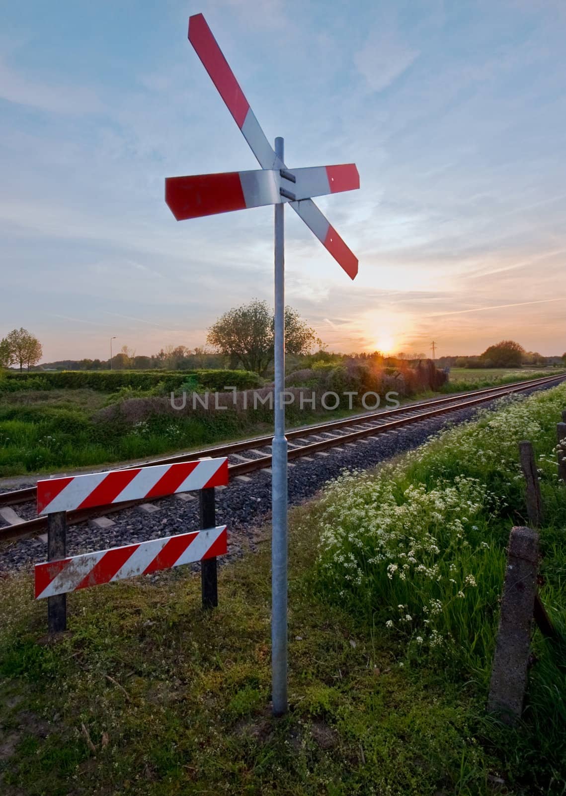 railway tracks with pastel sunset and traffic sign in a rural scene    by karinclaus