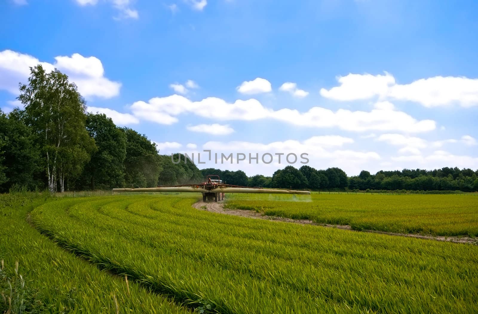bright green agriculture farmland with tractor sprinkle-sweeper installation with cloudy blue sky

