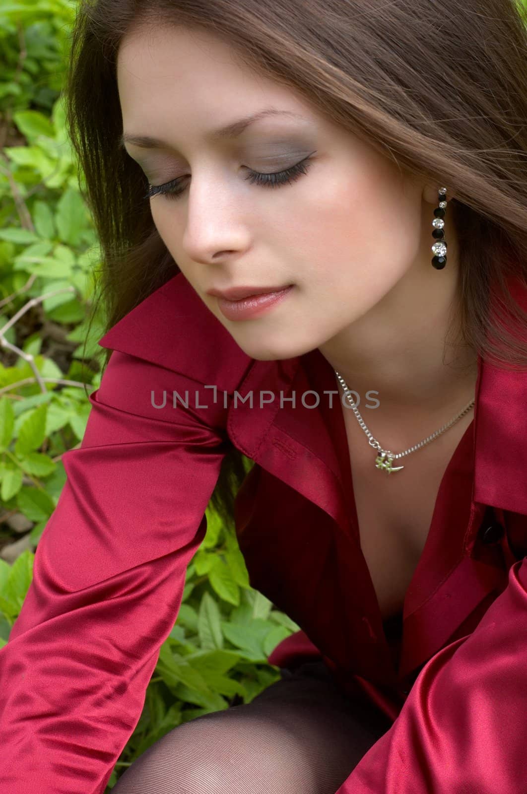 sexy brunette in red siting on the green foliage