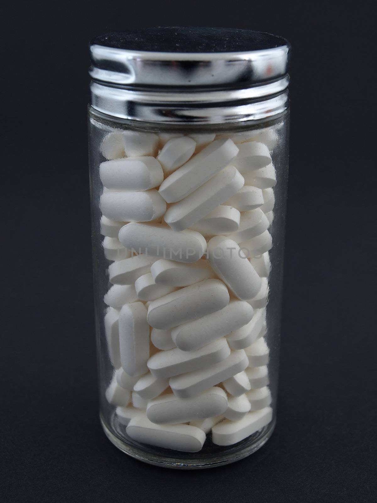 Large white pills in a glass jar, studio isolated against a black background.