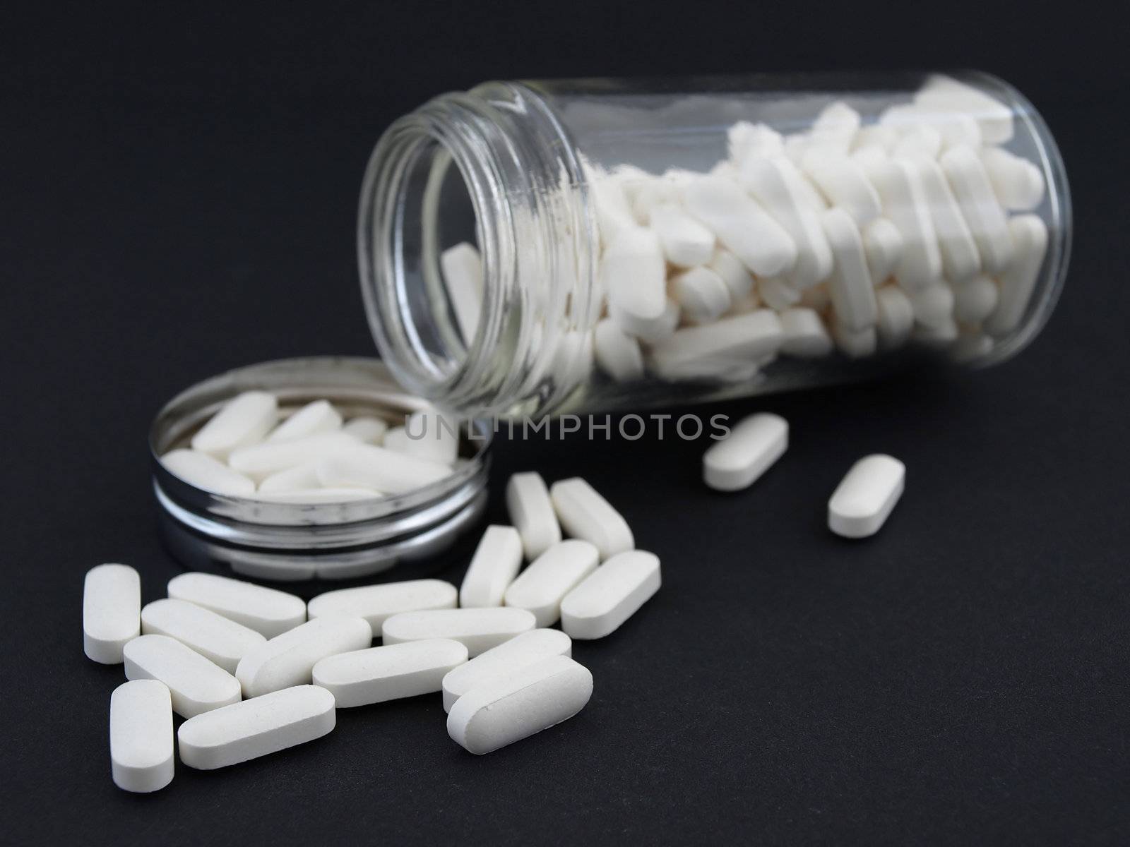 Large white pills spilling from a glass jar, studio isolated against a black background.