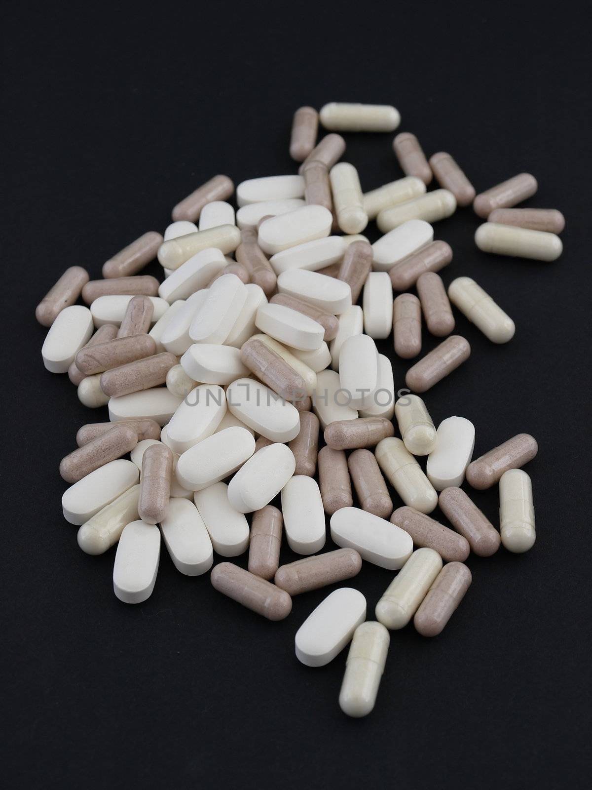 A spill of large white pills and brown capsules over a black background.