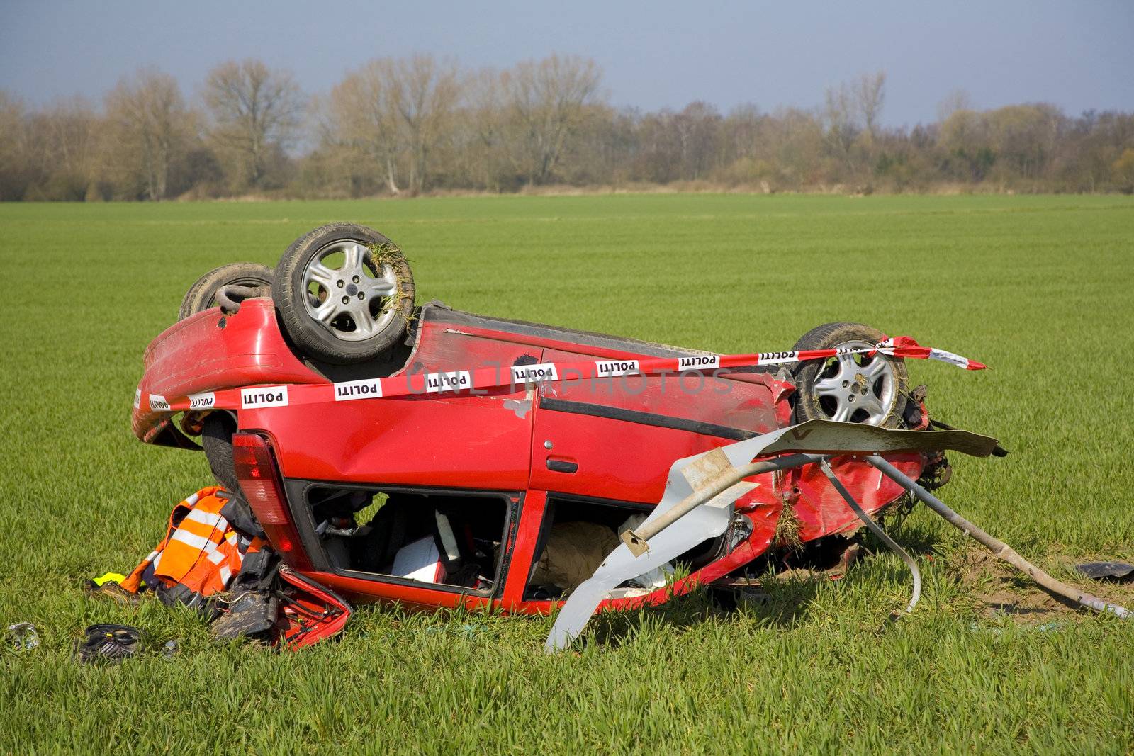 Crashed car in a field at springtime marked by the Danish police.