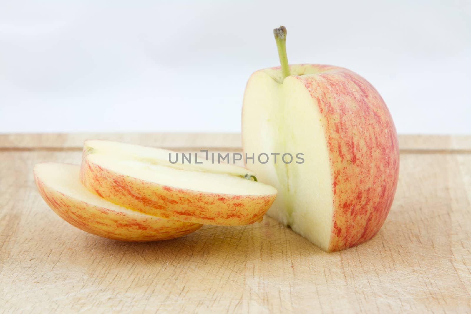 An apple sliced on a wooden chopping board with a white background.