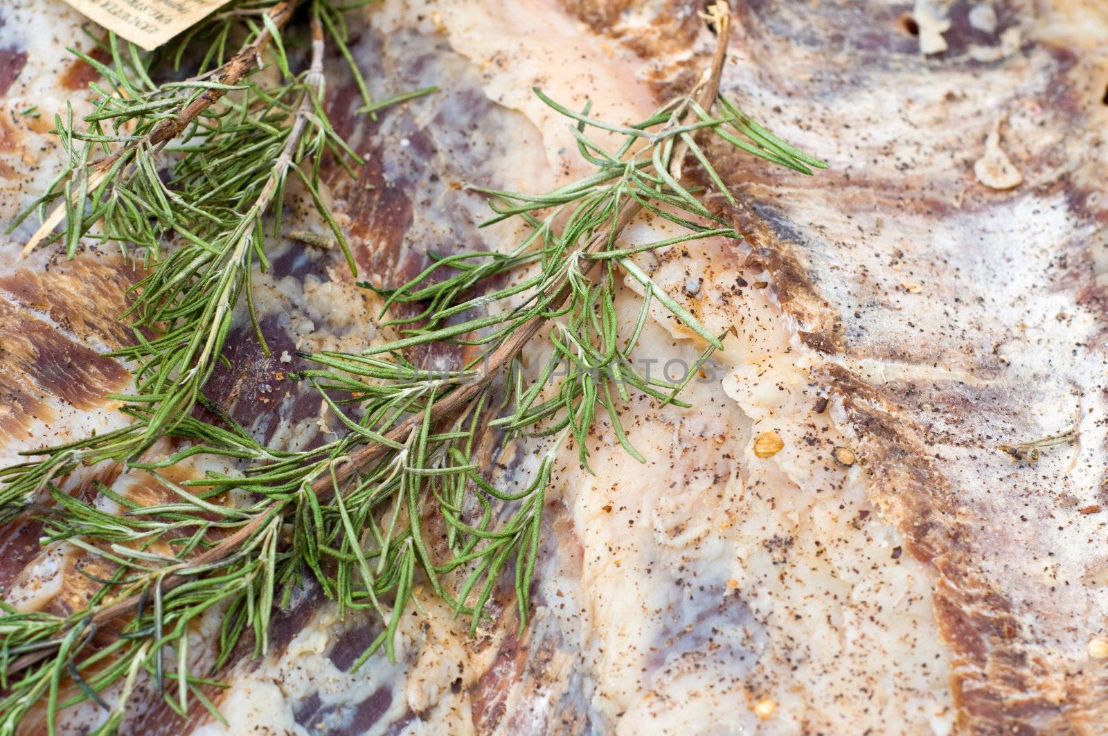 Close up shot of rosmary leaves on Italian salty lard. Lardo is a type of Italian charcuterie made  of fatback with rosemary and other herbs and spices. 