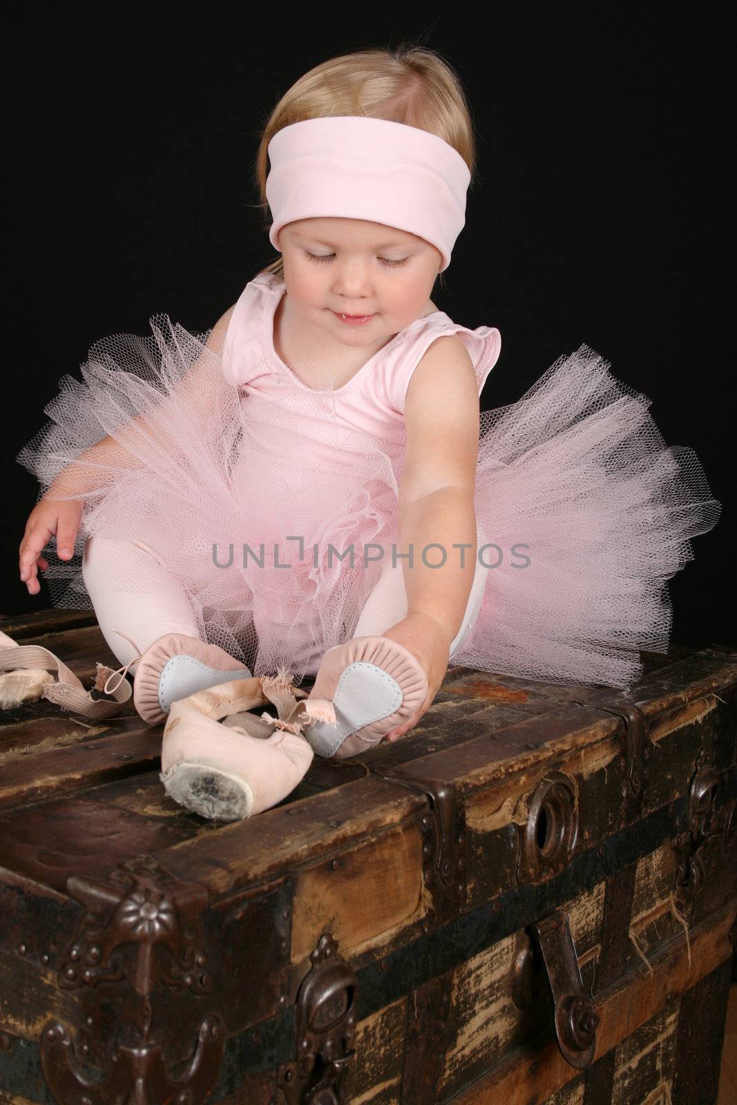 Blond toddler wearing a tutu holding Ballet shoes 