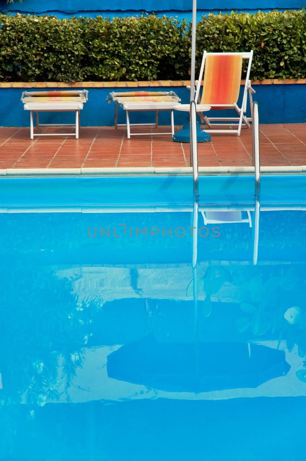 Hotel swimming pool with reflection and deck-chairs. Shallow depth of field.