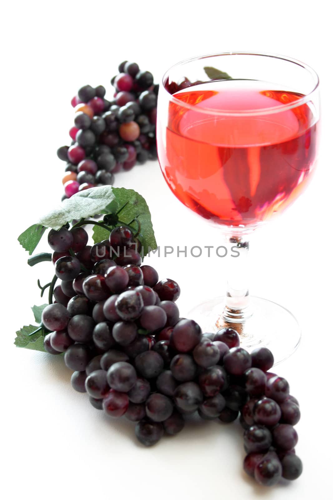 A glass of red wine with grapes all on a high key background.