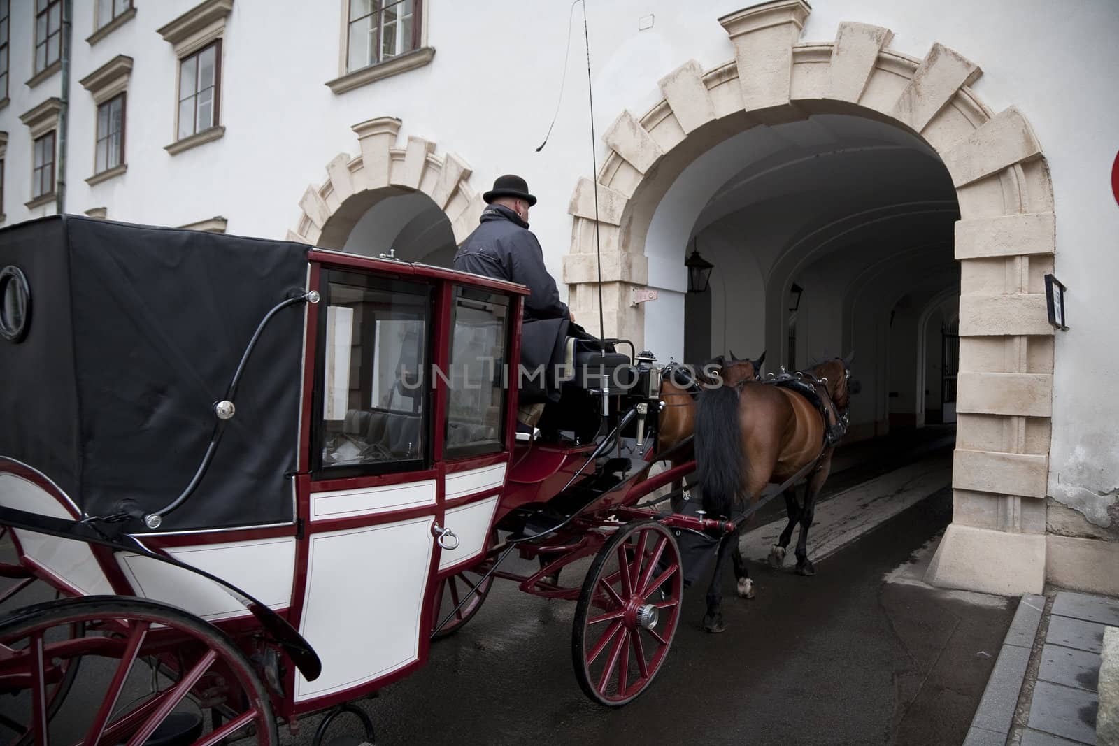One of the famous horse cabs of Vienna, Austria driving though the gateway of Hofburg Castle. 