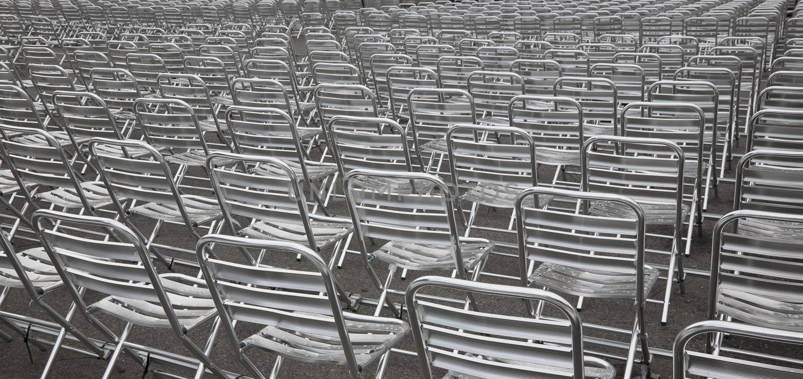 Rows of empty metal chairs after rain at an outdoor urban arena at summertime.