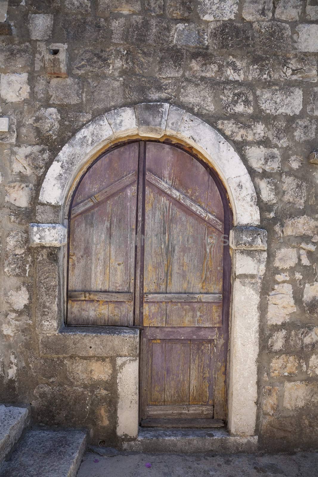 Nice old shuttered entrance in stone wall seen in steep Croatian alley.