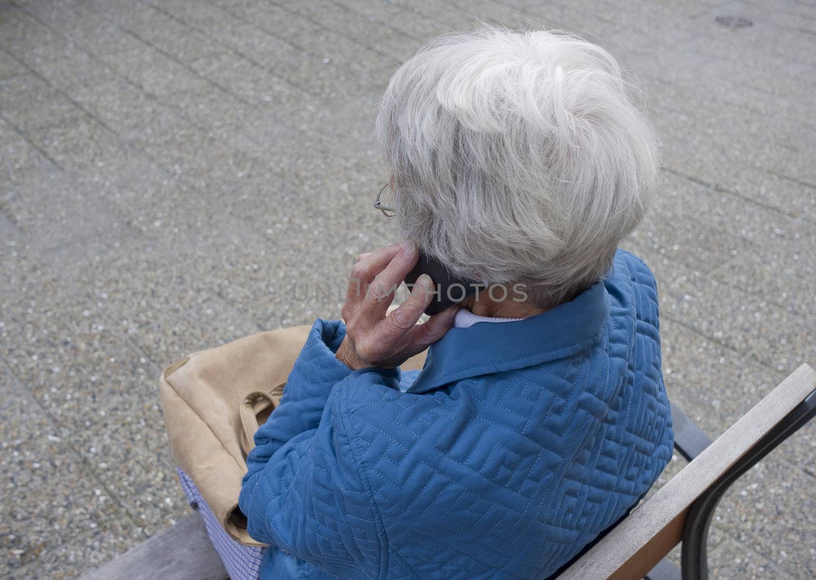 Female senior talking in cell phone on a public bench.
