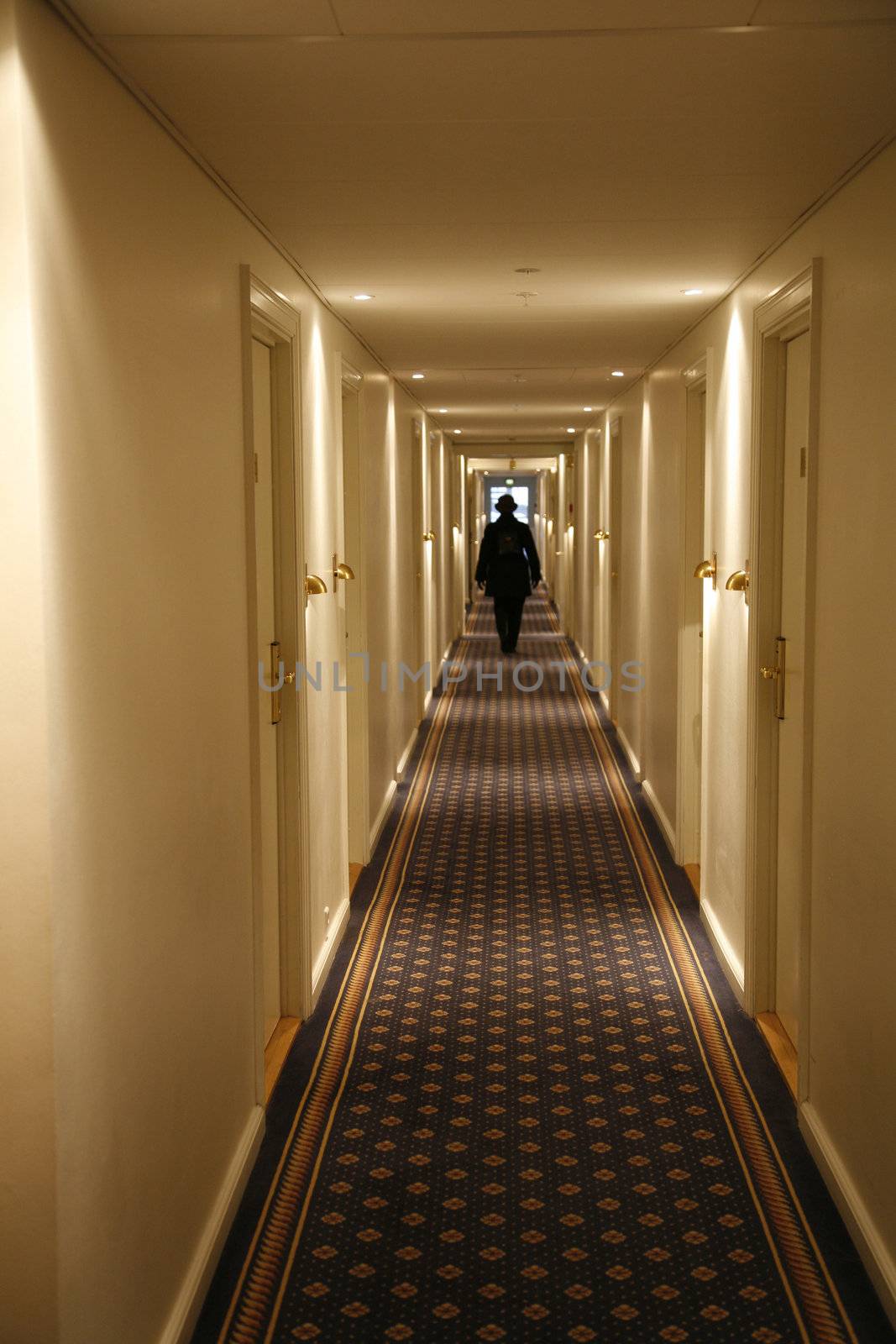 Black dressed person walking down a long hotel corridor. Motion blur.