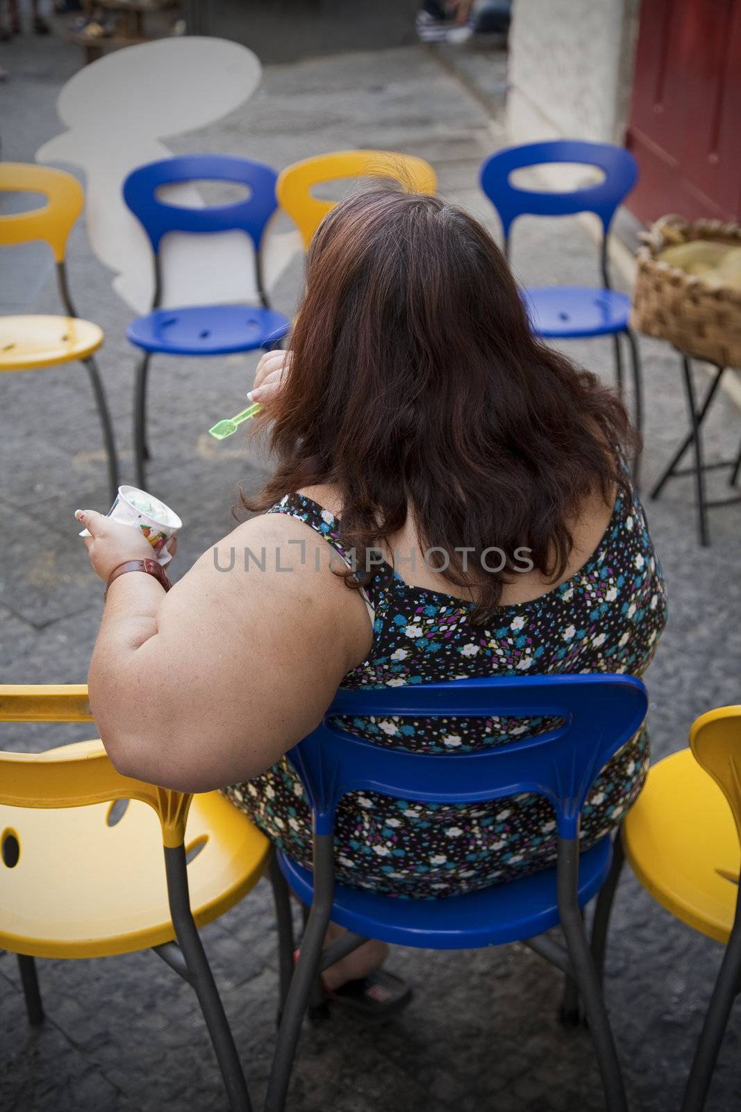 Adult overweight female sitting outdoors eating an icecream.