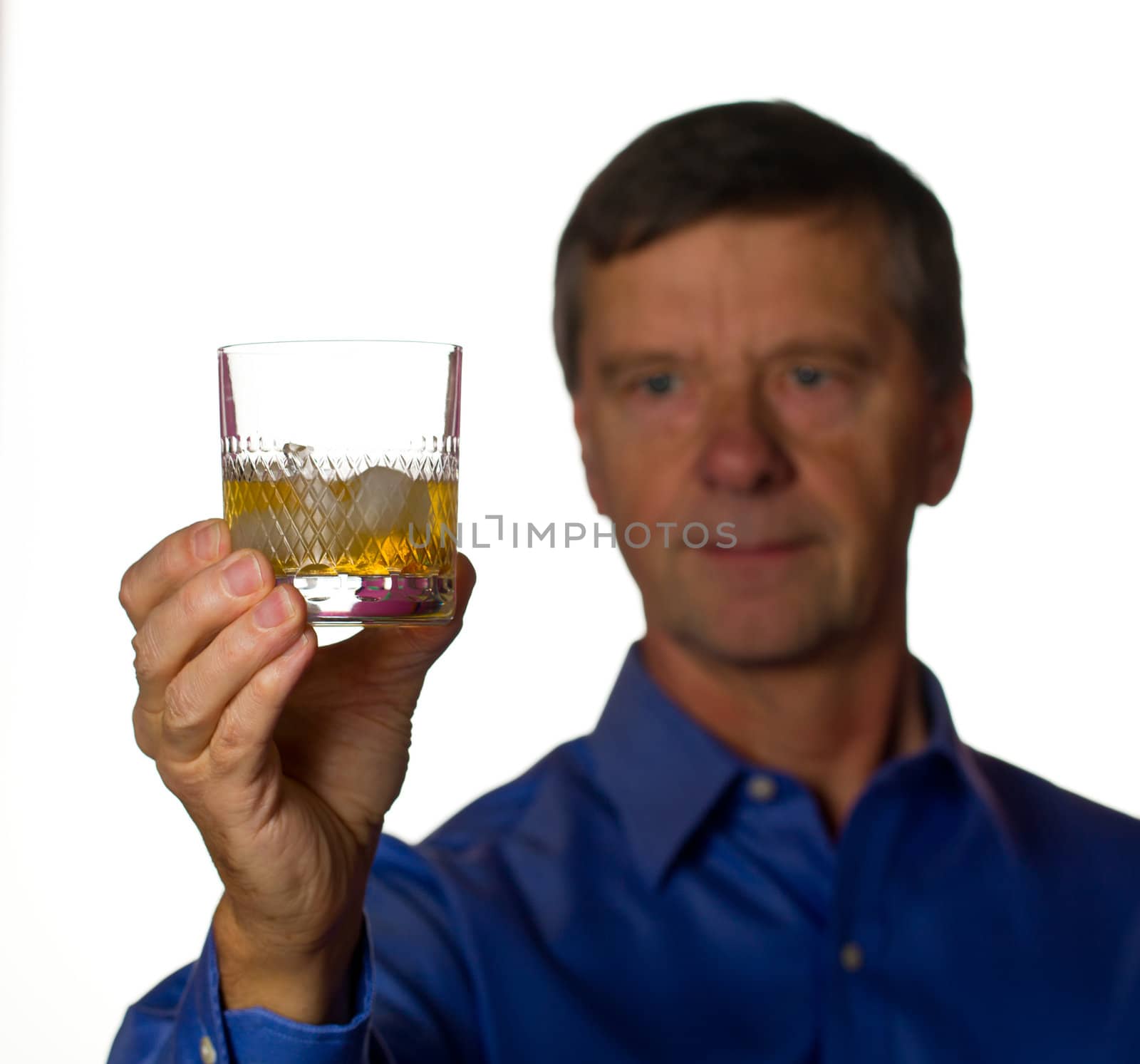 Senior retired male with a glass of scotch whiskey on ice in a cut glass with the man out of focus