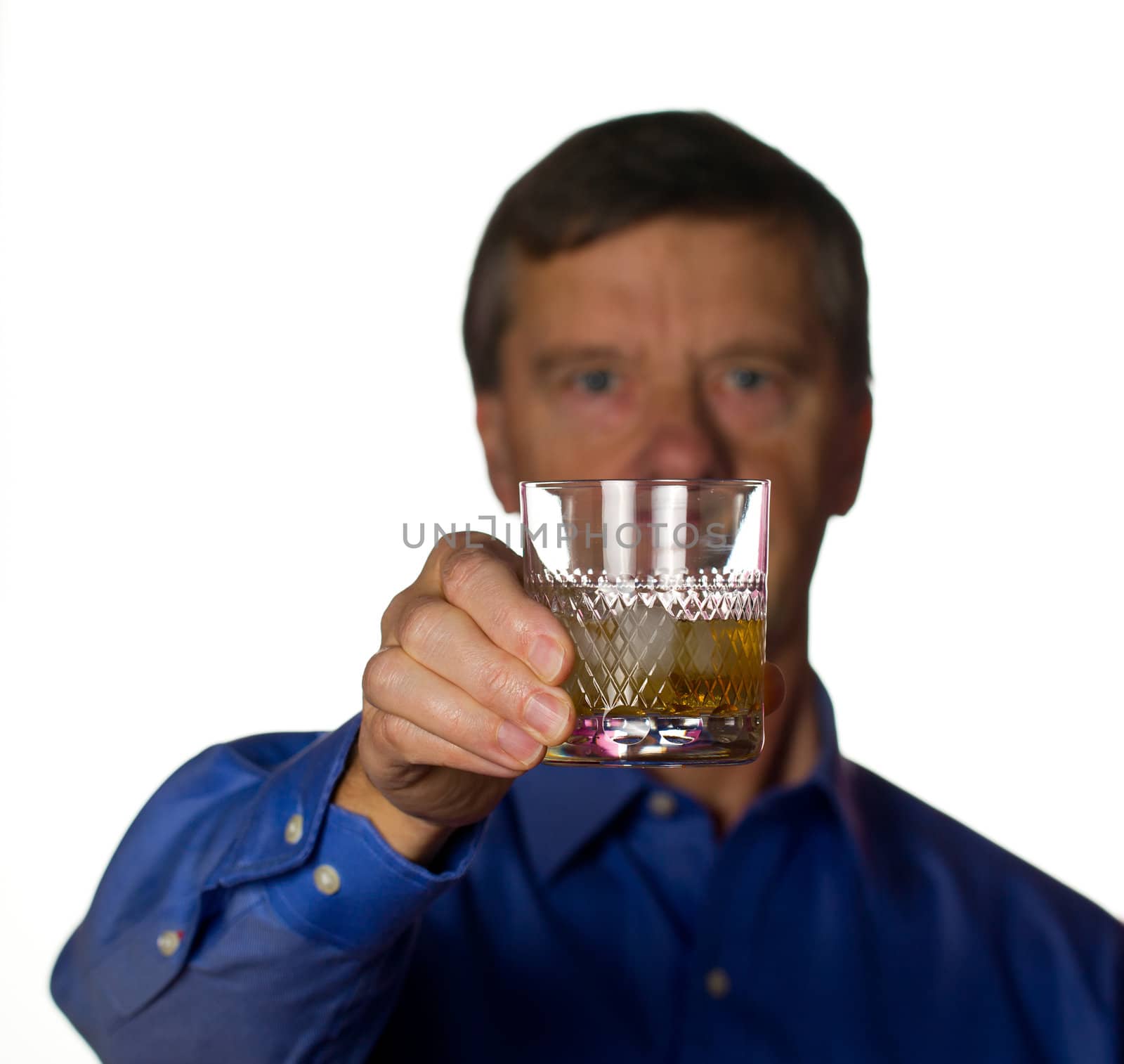 Senior retired male with a glass of scotch whiskey on ice in a cut glass with the man out of focus