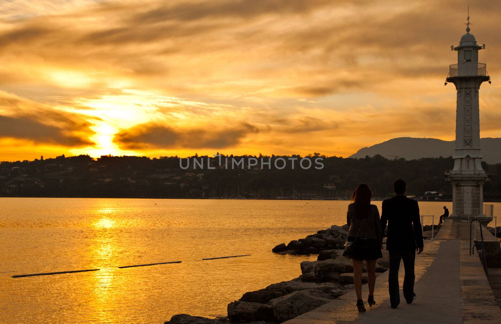 Couple silhouetted walking along a pier at Lake Geneva, Switzerland toward the lighthouse
