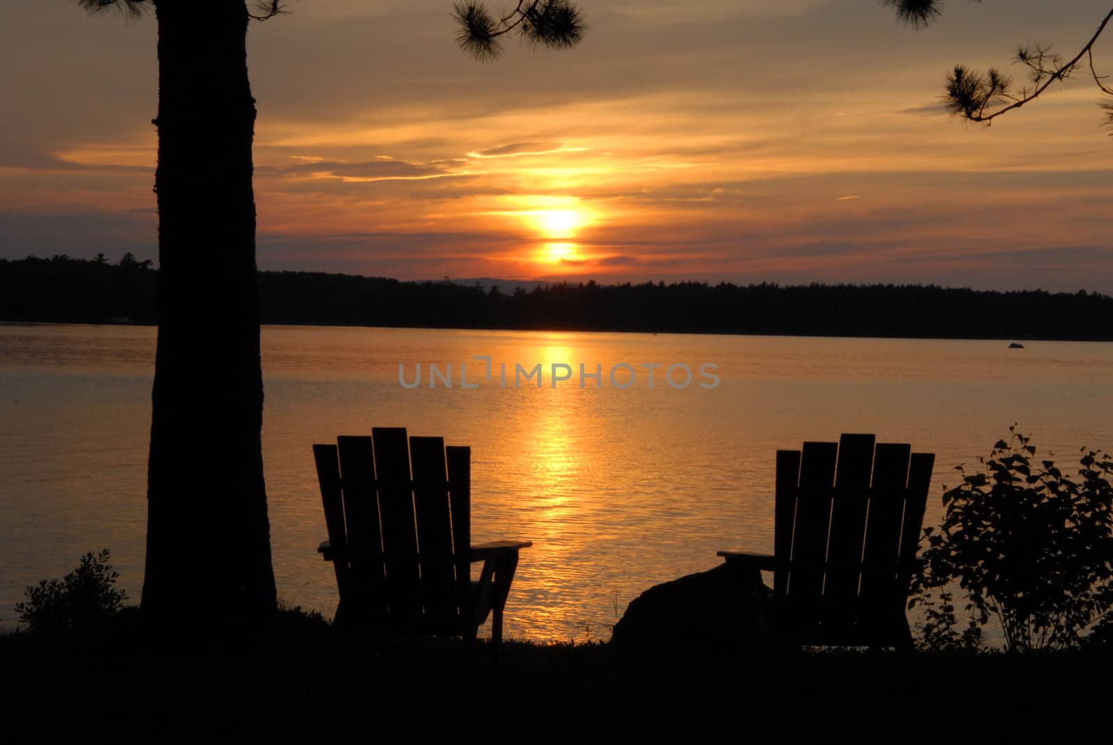 Sunset over Lake Millinocket in Maine with two chairs for viewing.