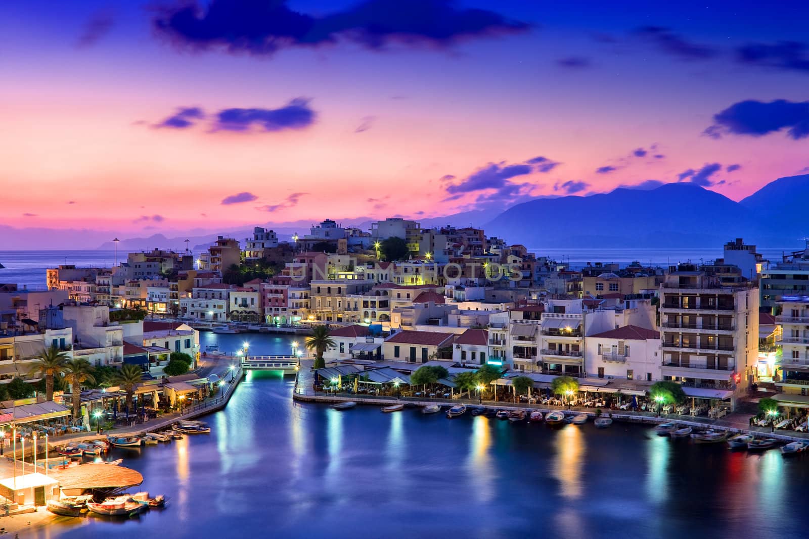 Agios Nikolaos. Agios Nikolaos is a picturesque town in the eastern part of the island Crete built on the northwest side of the peaceful bay of Mirabello.