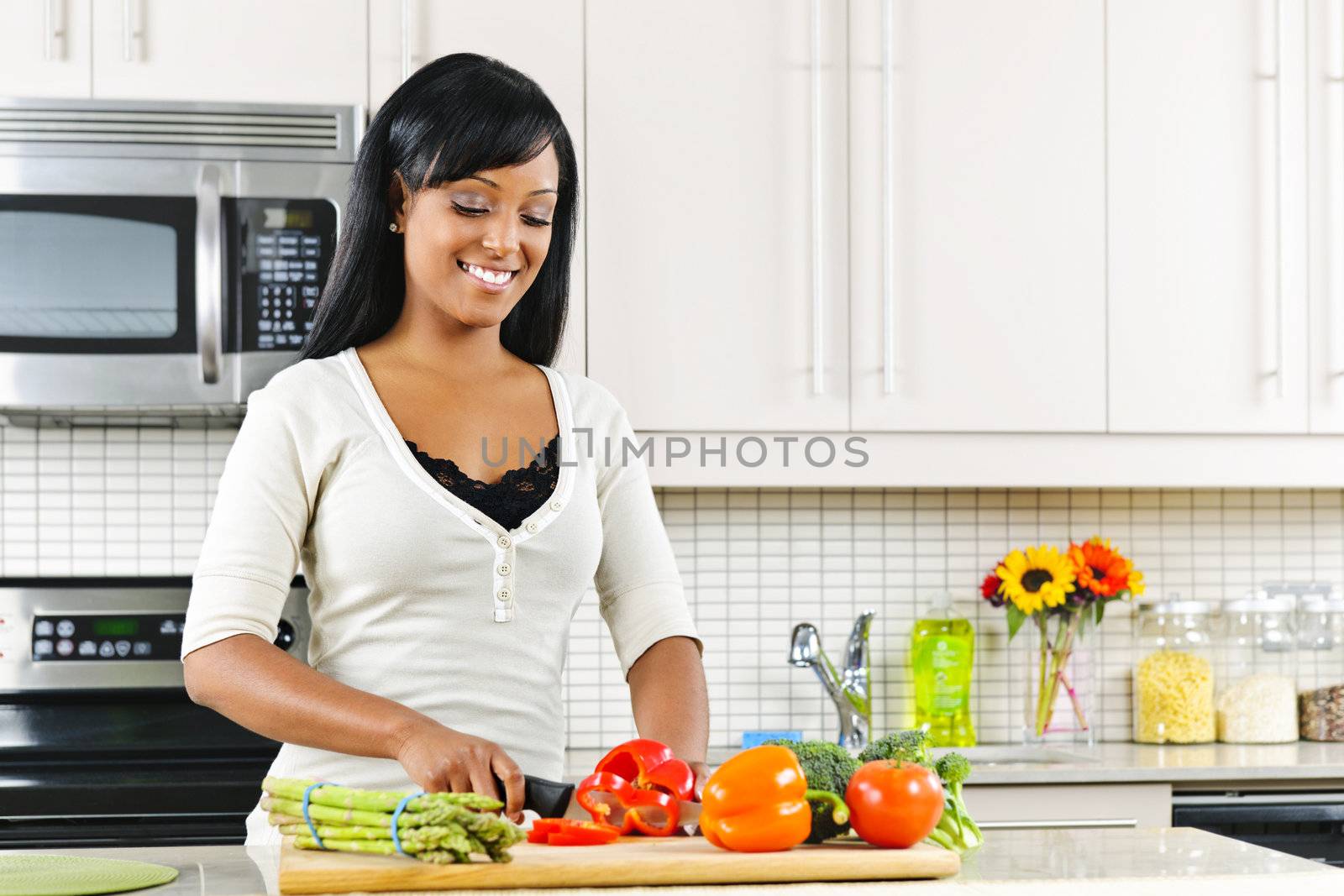 Young woman cutting vegetables in kitchen by elenathewise