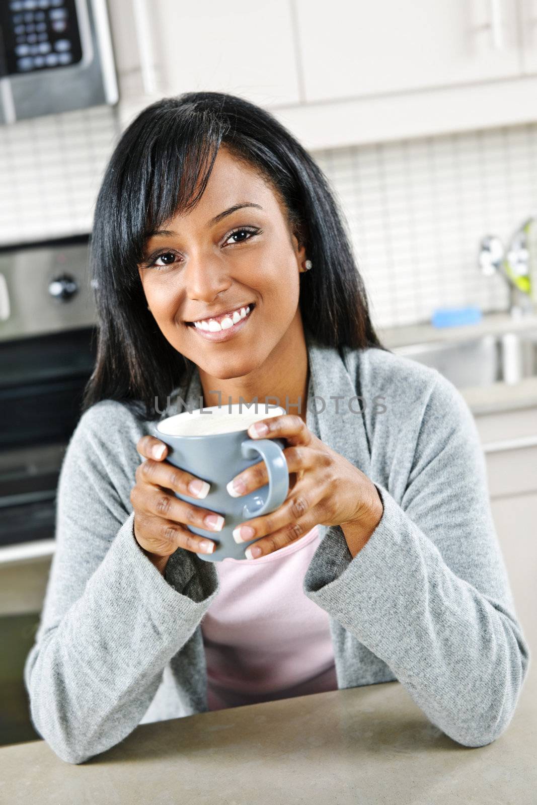 Smiling black woman holding coffee cup in modern kitchen interior