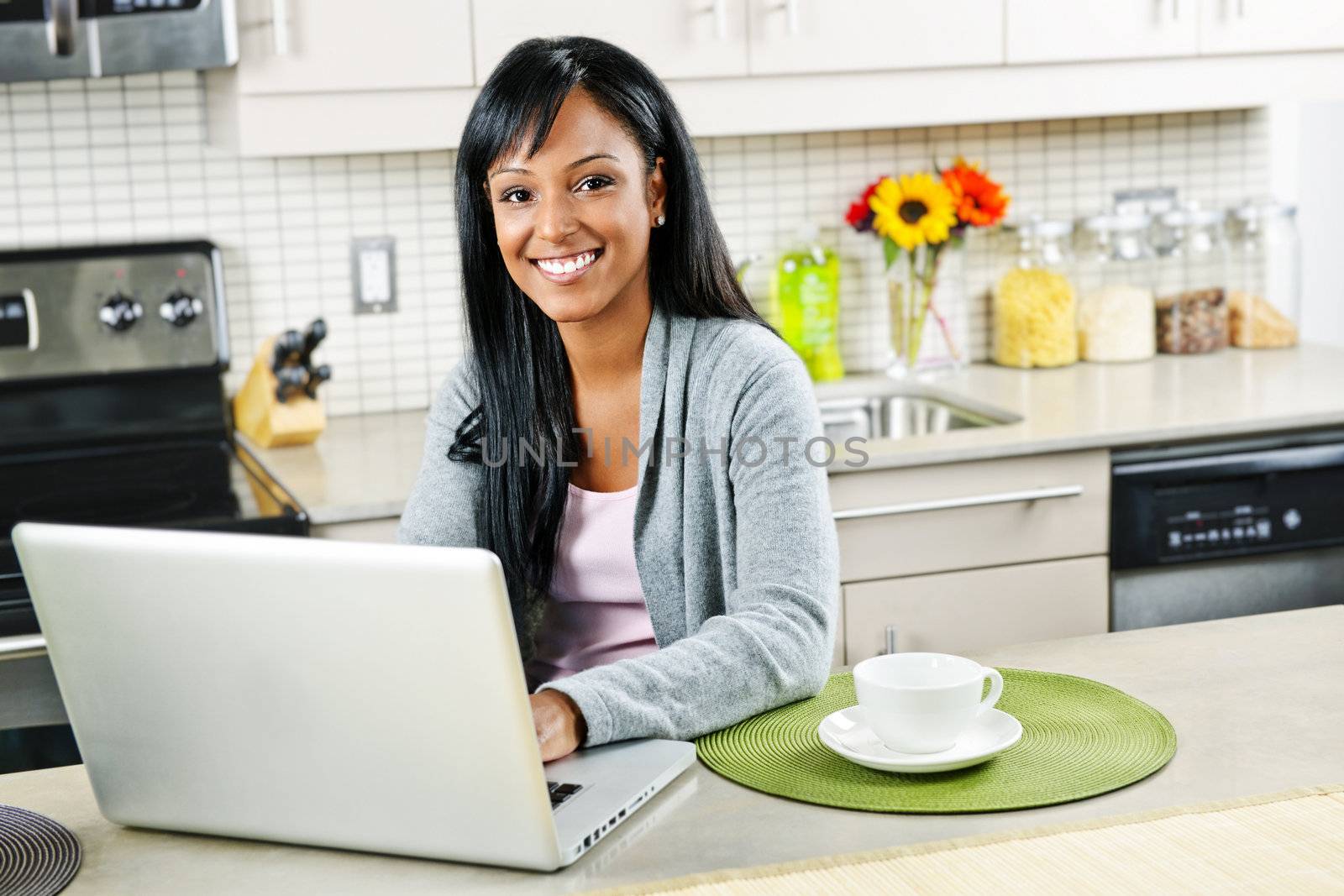 Smiling black woman using computer in modern kitchen interior