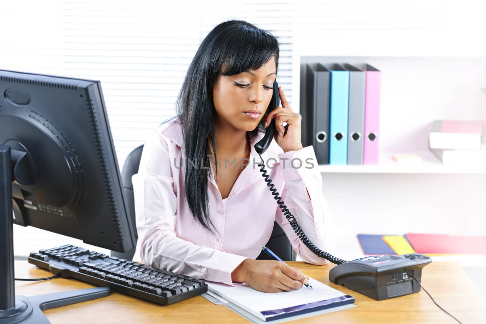 Serious black businesswoman on phone at desk by elenathewise