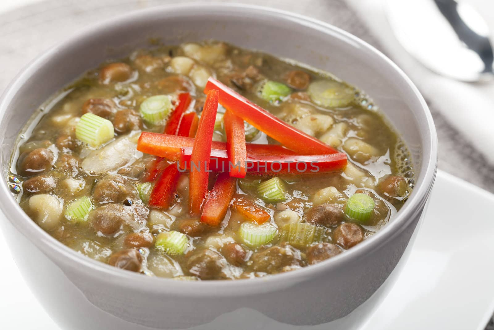 Bowl of fresh soup with kapucijners, green onions, and red bell pepper garnish