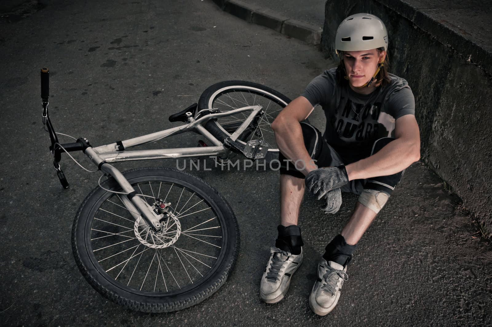 Extreme biker sitting on asphalt and relaxing