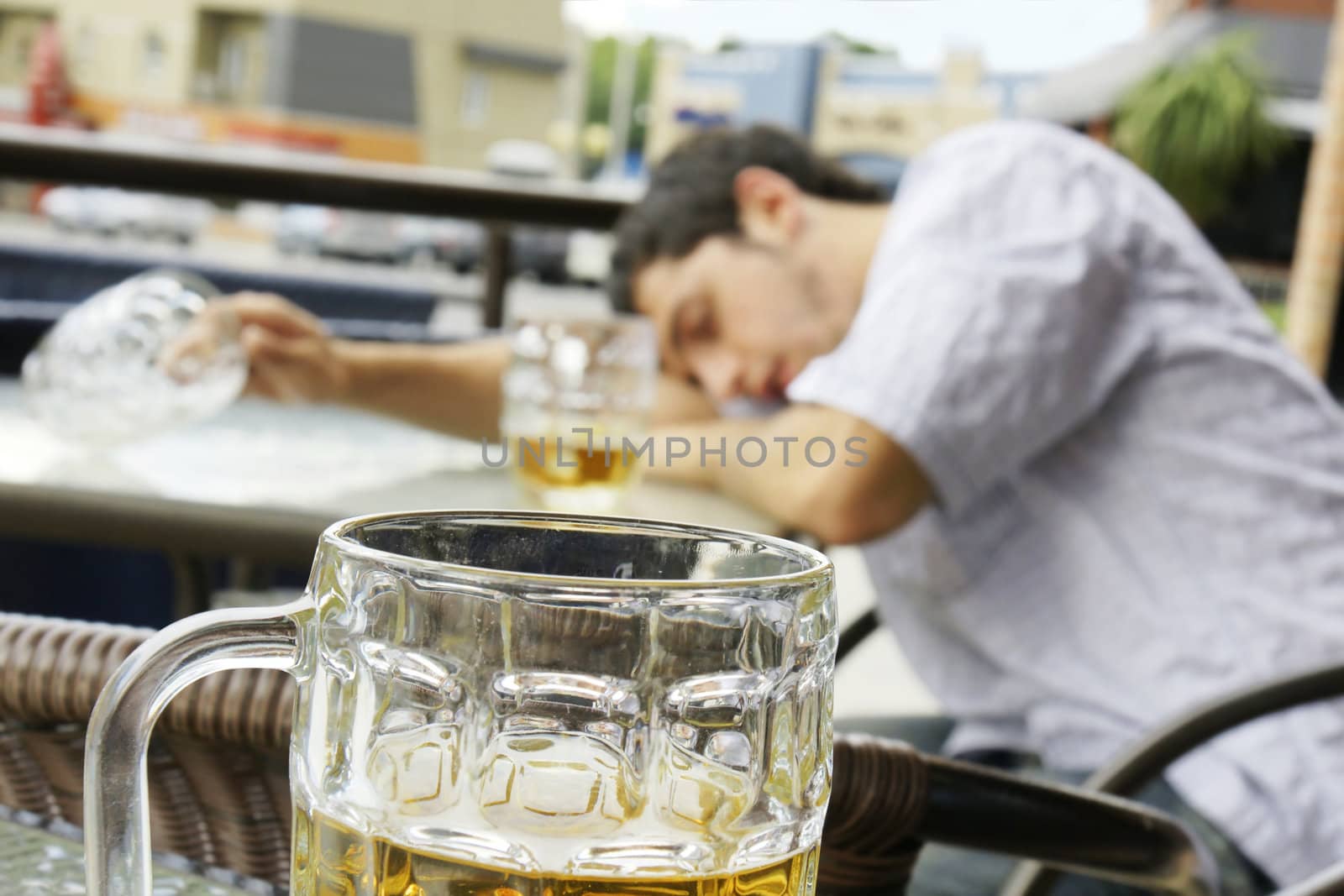 Alcohol abuse: drunk young man or student lying down on a table with beer bock still in hand, focus on glass up front.