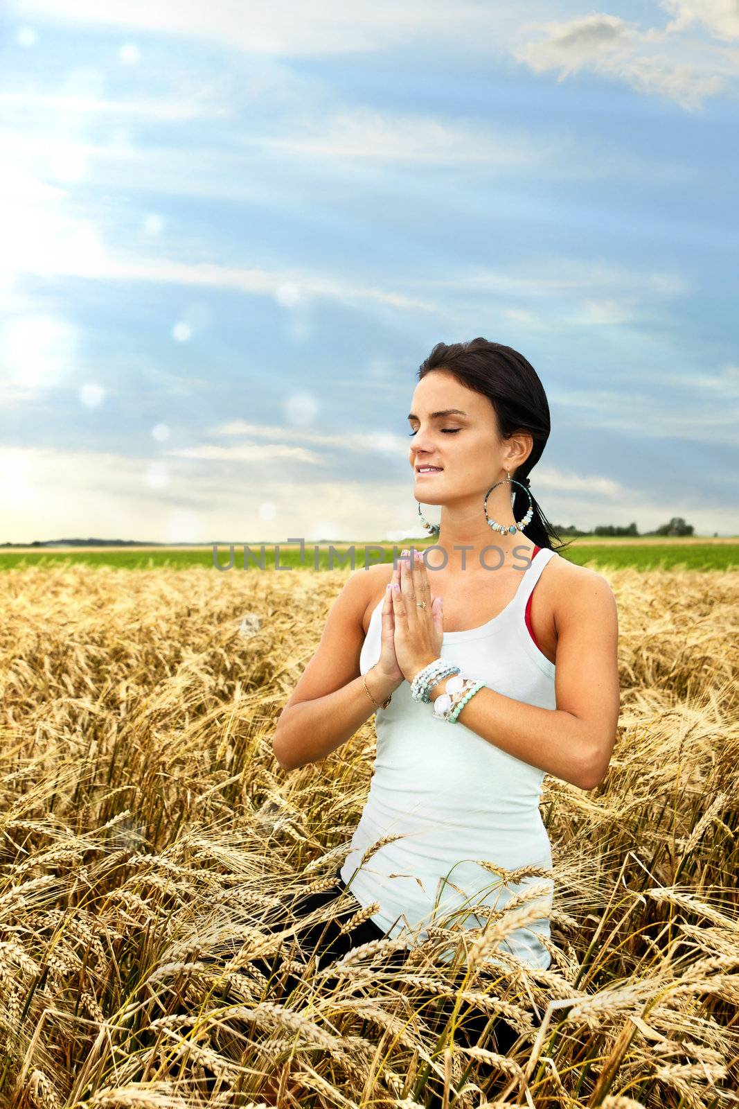 Beautiful healthy young woman connecting with nature by doing yoga and medidating at dawn in a ripe wheat field.