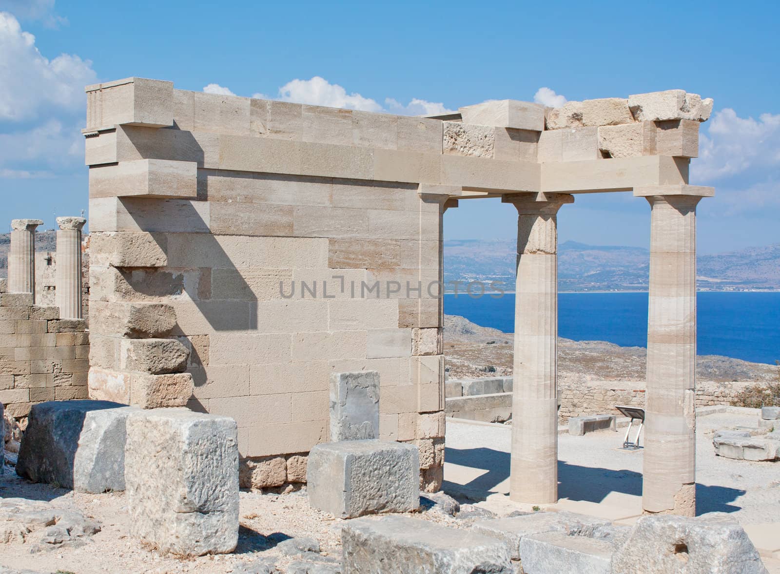 Restored and original pieces of the ancient Greek temple of Athena Lindia on the Acropolis of Lindos in the Dodecanese island of Rhodes, Greece, with the Aegean Sea in the background.