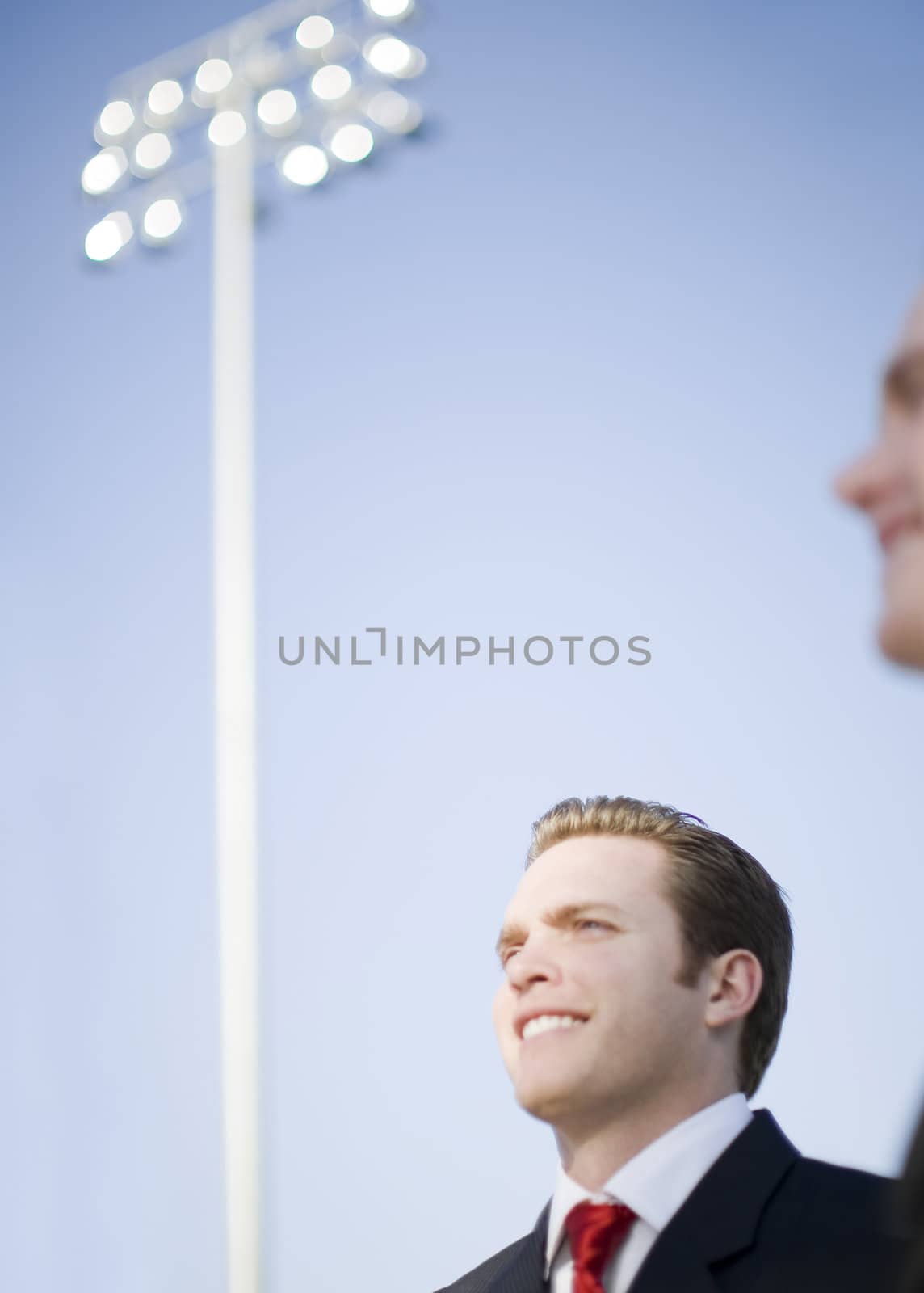 two business people smiling outside standing in a stadium with large lights in the bacground under a blue sky
