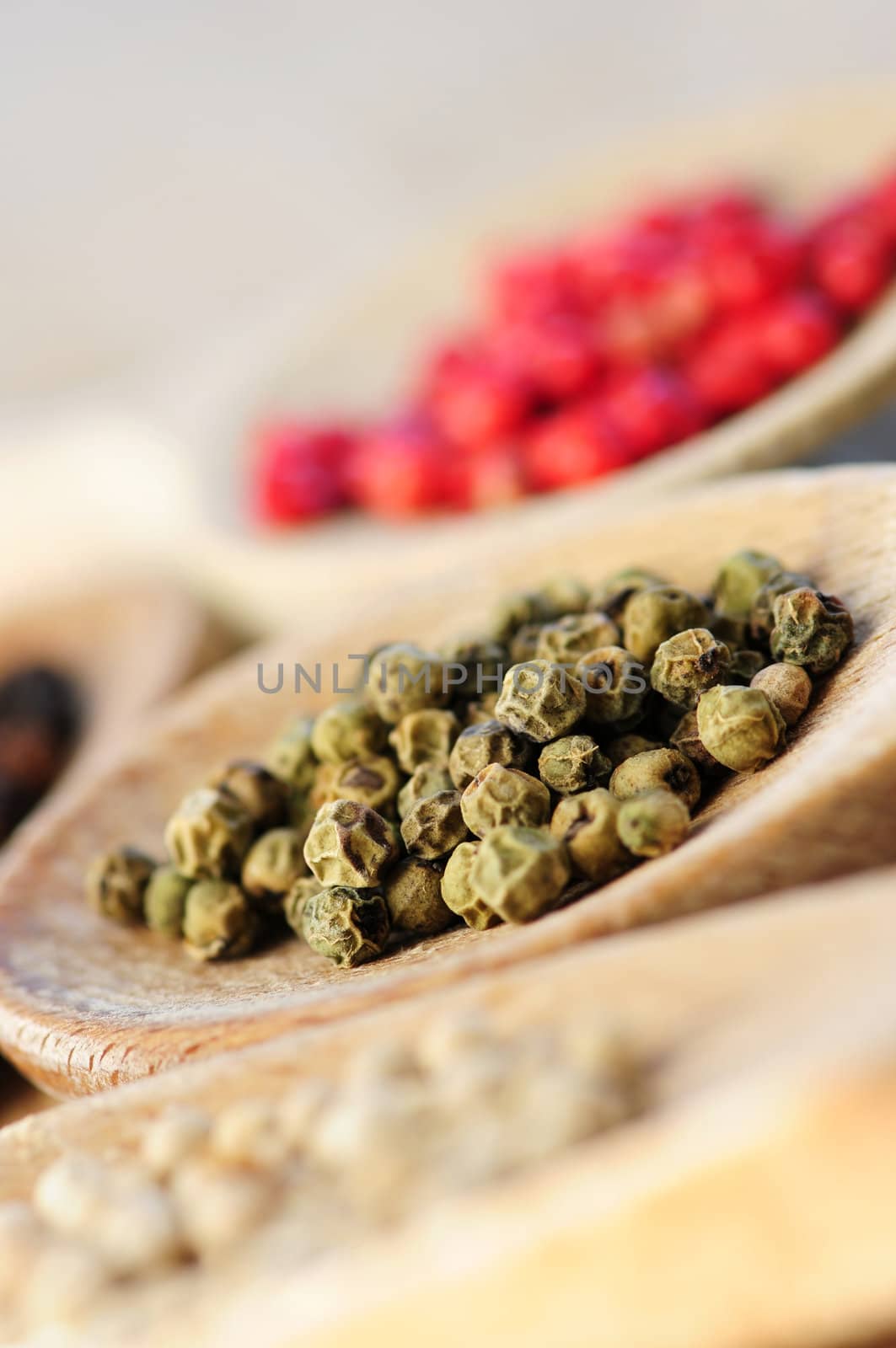 Different kinds of peppercorns in wooden cooking spoons macro