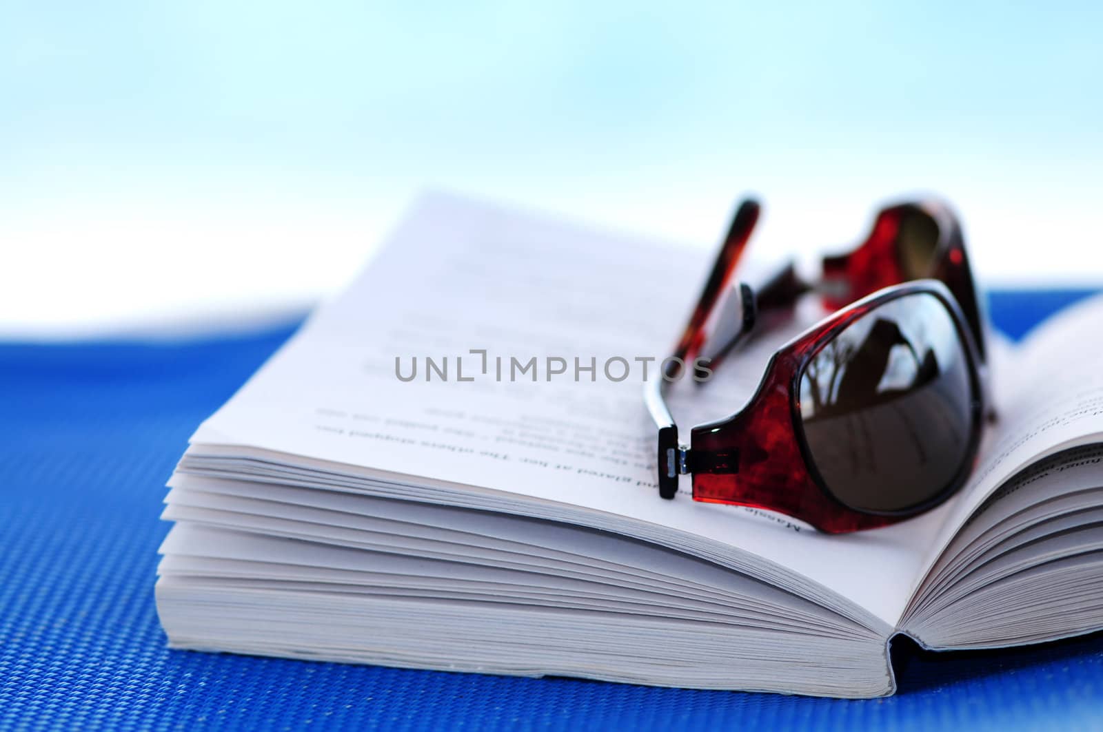 Sunglasses and open book on beach chair - summer vacation concept