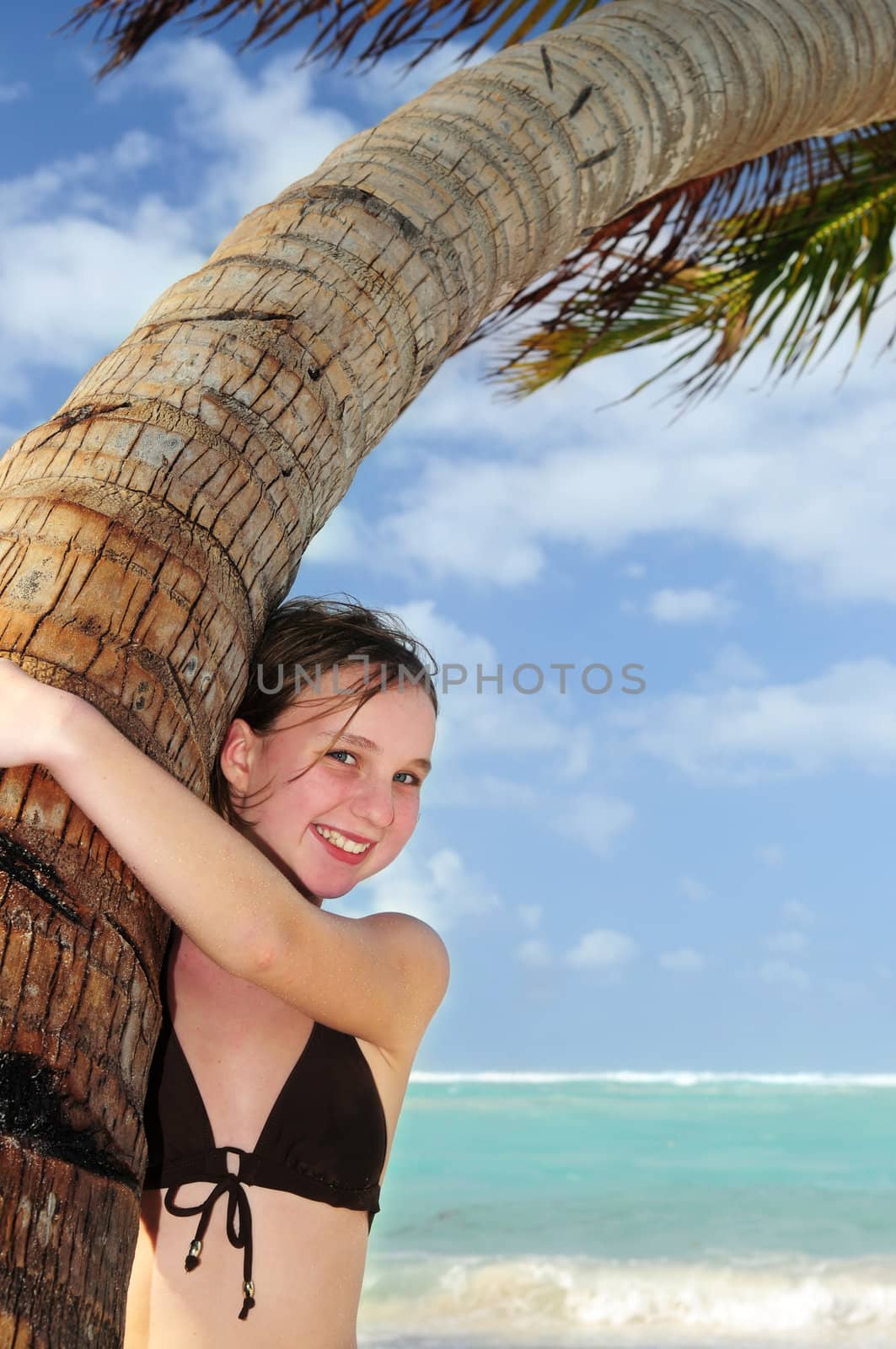 Happy young girl higging a palm tree on tropical beach
