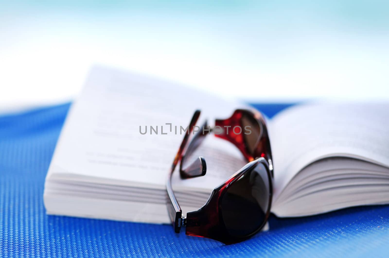 Sunglasses and open book on beach chair - summer vacation concept